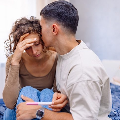 A young Caucasian woman feeling sad and disappointed because of the negative pregnancy test and her partner is trying to comfort her